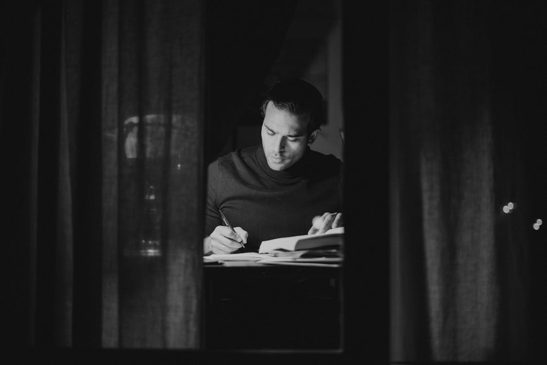 Free Pensive man writing in notebook and reading book Stock Photo