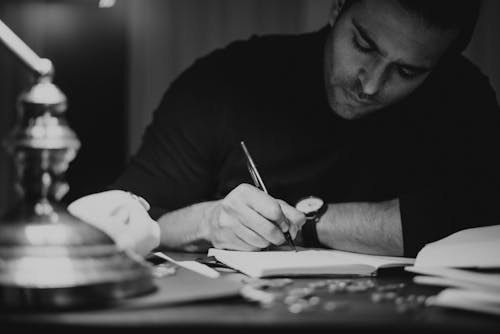 Free Crop man taking notes in copybook in dark home office Stock Photo