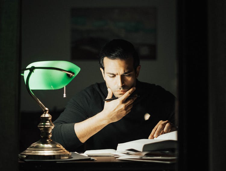 Frowning Man Reading Book And Taking Notes In Home Office