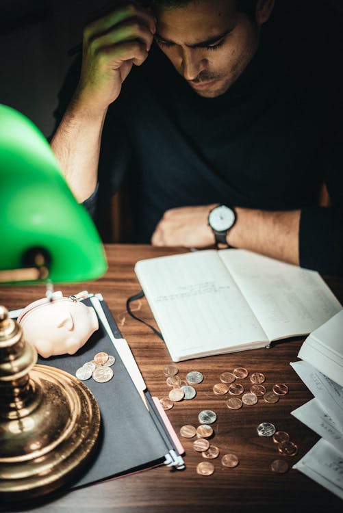 Free High angle of concentrated man at table with retro lamp and coins contemplating on notes in journal Stock Photo