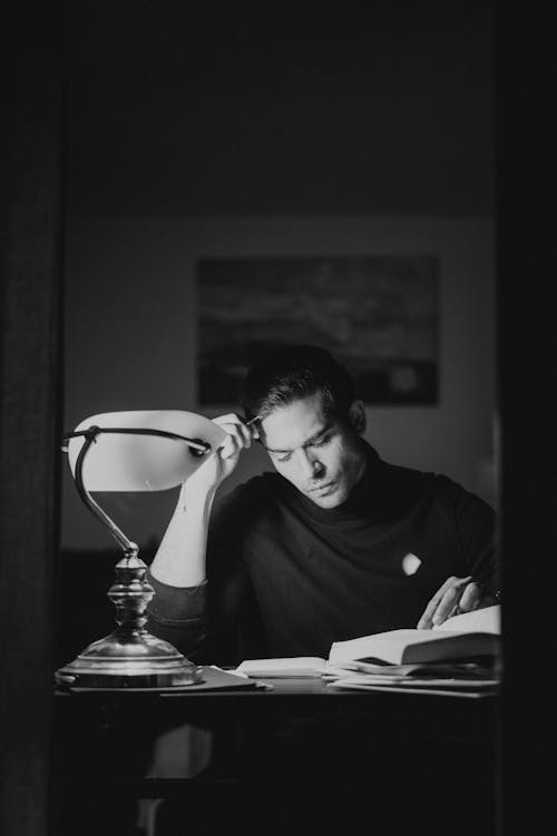 Thoughtful man with books at desk in night