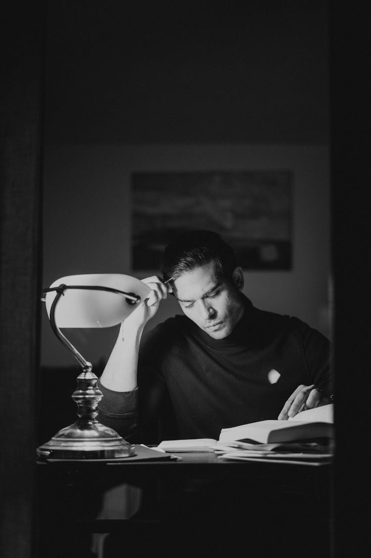 Thoughtful Man With Books At Desk In Night