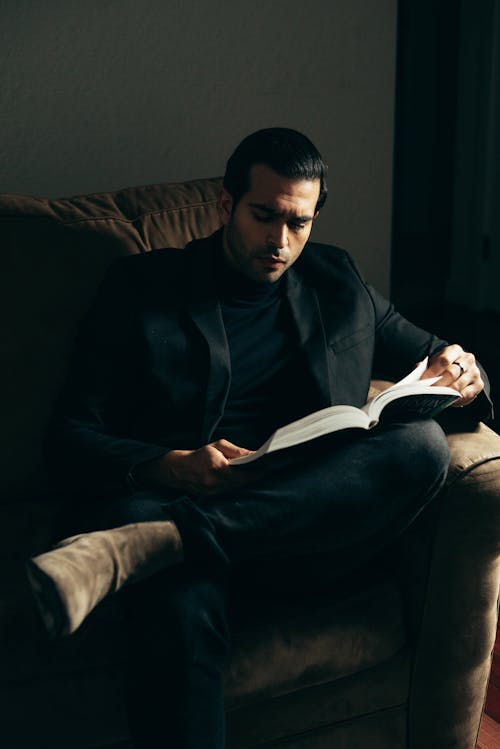 Serious formal man reading book on couch