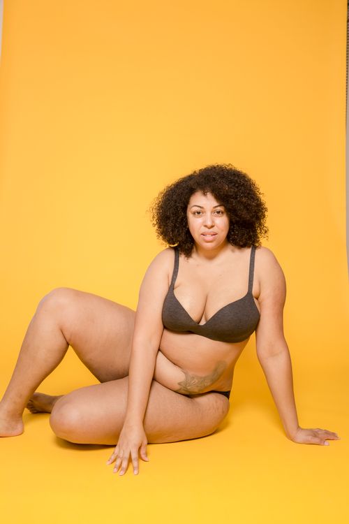 Free Adult plus size ethnic female in lingerie with curly hair and tattoo sitting on floor while looking at camera Stock Photo