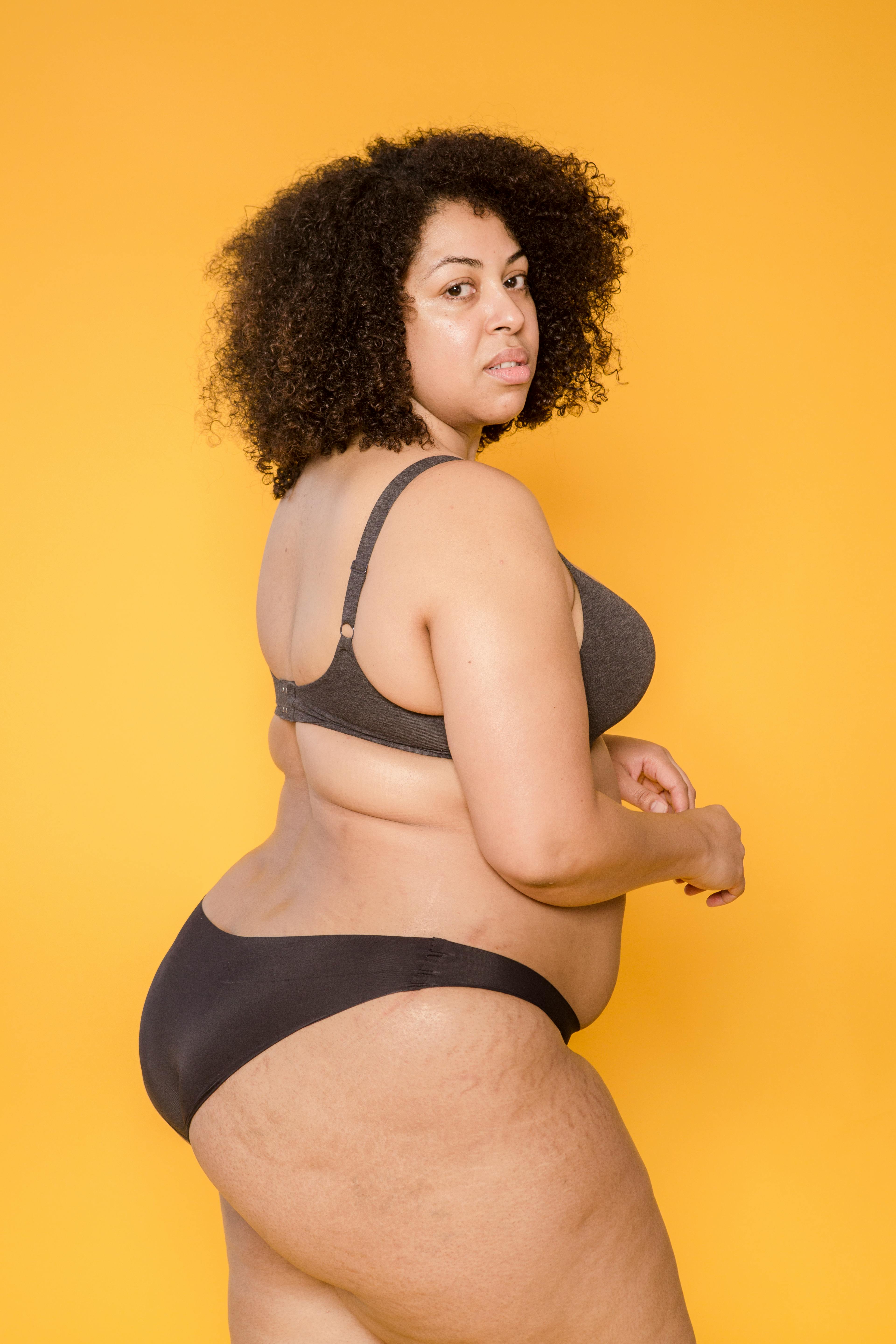 Attractive African American overweight female model with long curly hair  wearing delicate lace bra looking at camera against yellow background stock  photo - OFFSET