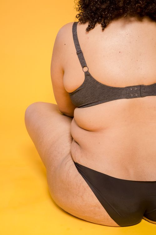 Free Back view of crop unrecognizable voluptuous woman in bra and panties with curly hair sitting on floor Stock Photo
