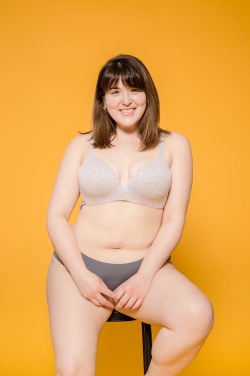 Cheerful overweight Asian model in underclothes on yellow background