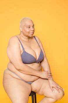 Portrait of a confident plus size woman in underwear, exuding strength on a yellow background.