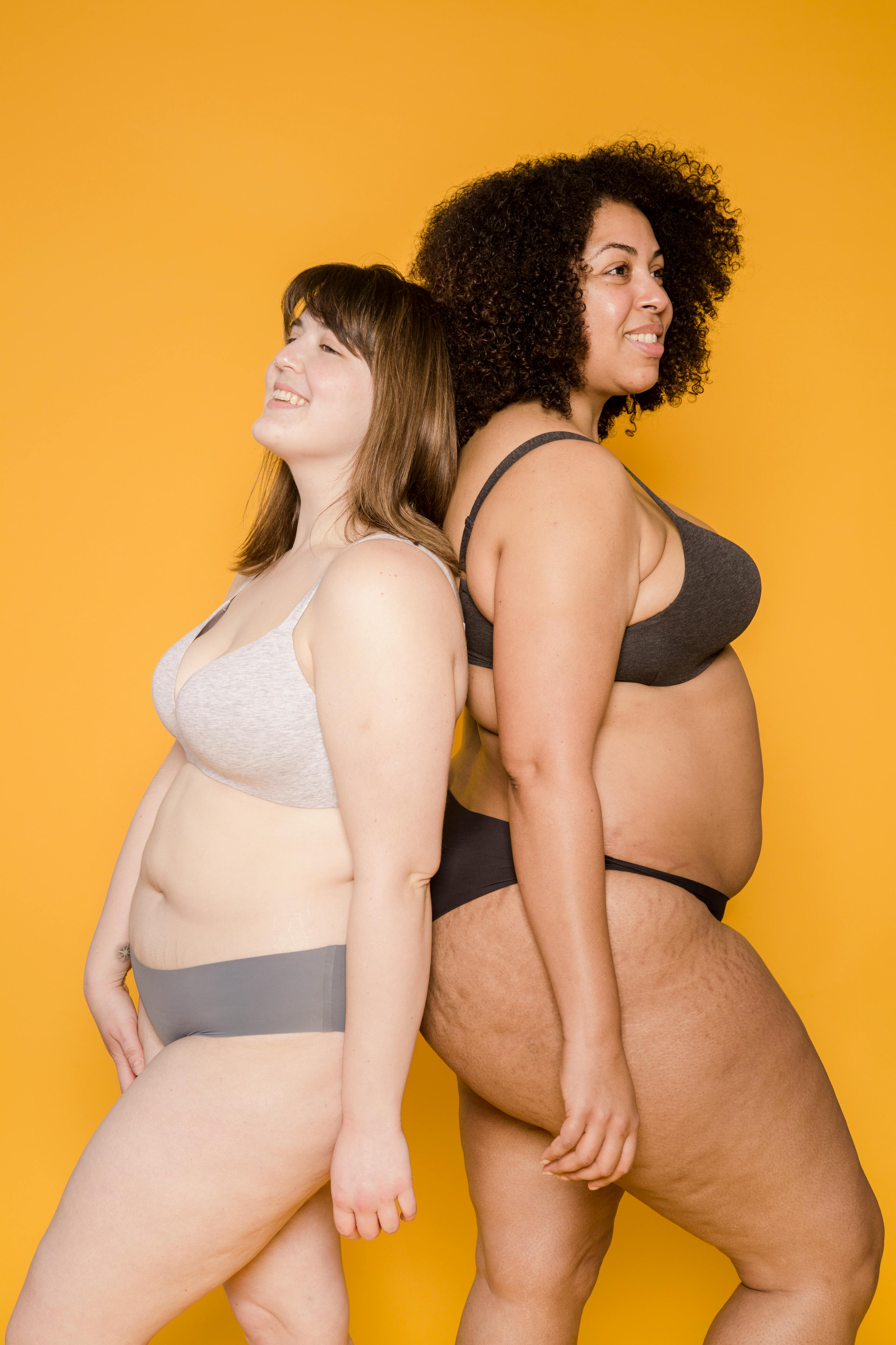 Crop plump multiethnic models in underclothes on light background