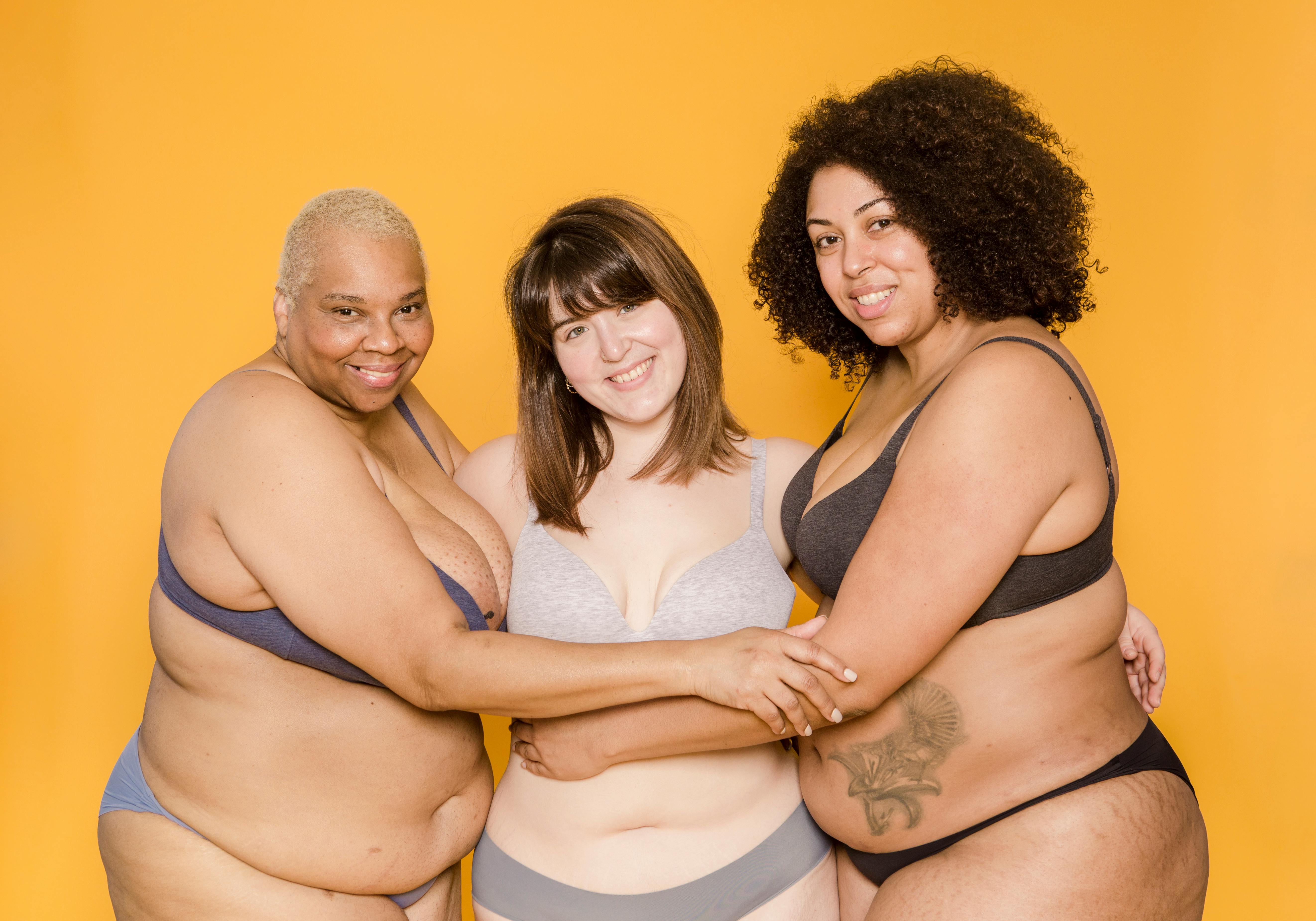 Cheerful plus size multiracial girlfriends in lingerie on yellow