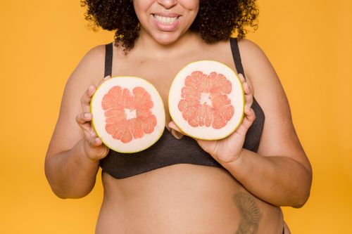 Free Crop anonymous smiling plump African American female in bra with cut juicy grapefruit and tattoo on yellow background Stock Photo