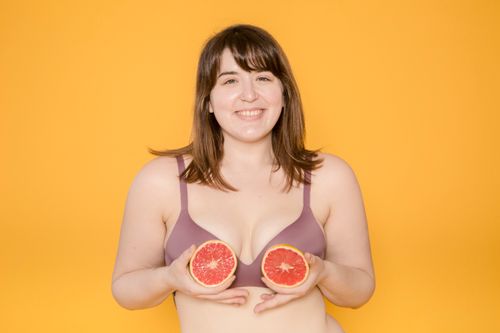 Free Cheerful plus size ethnic woman in bra with fresh grapefruit halves looking at camera on yellow background Stock Photo