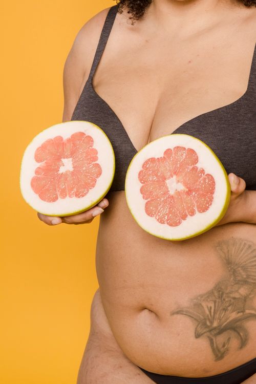 Free Crop anonymous plus size woman in underwear with tattoo and juicy grapefruit halves on yellow background Stock Photo