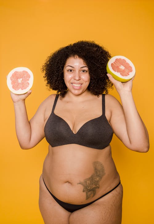 Smiling overweight ethnic model in lingerie with grapefruit halves