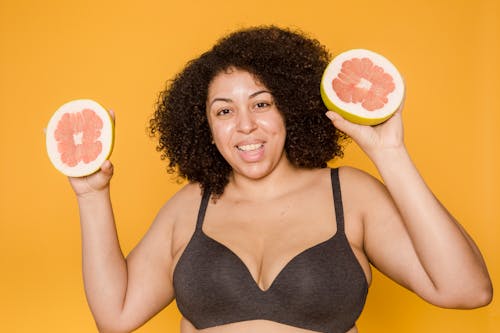 Smiling overweight ethnic woman in brassiere with fresh grapefruit halves