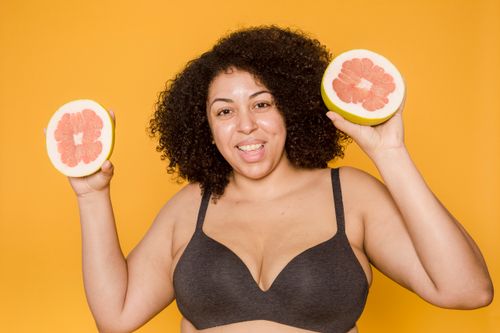 Free Cheerful plus size African American female in bra with curly hair and cut juicy grapefruit looking at camera on yellow background Stock Photo