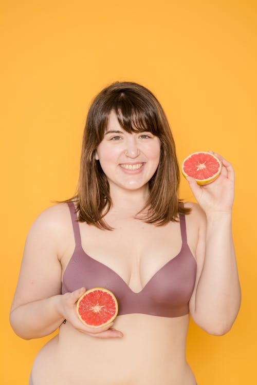 Cheerful plump Asian model in bra with grapefruit halves