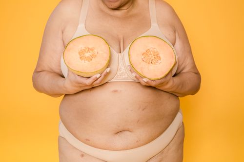 Free Crop unrecognizable voluptuous female model in bikini and brassiere with fresh melon halves on yellow background Stock Photo
