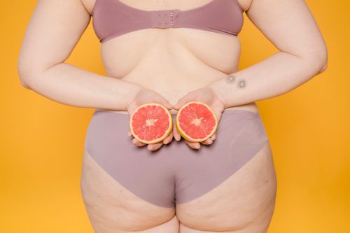 Free Back view of crop anonymous plus size woman in panties and bra with juicy grapefruit halves on yellow background Stock Photo
