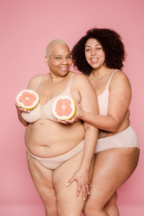 Free Cheerful overweight African American women wearing lingerie looking at camera on pink background with halves of ripe grapefruit in hands Stock Photo
