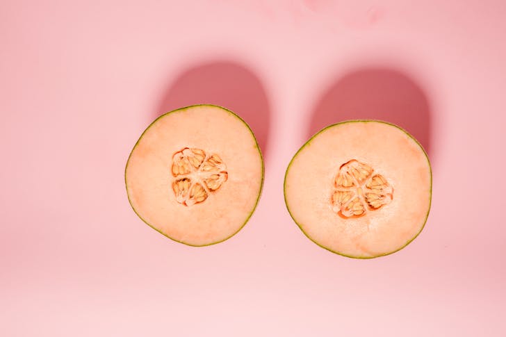 Top view of ripe orange melon cut into halves for healthy diet placed on pink background in modern light studio