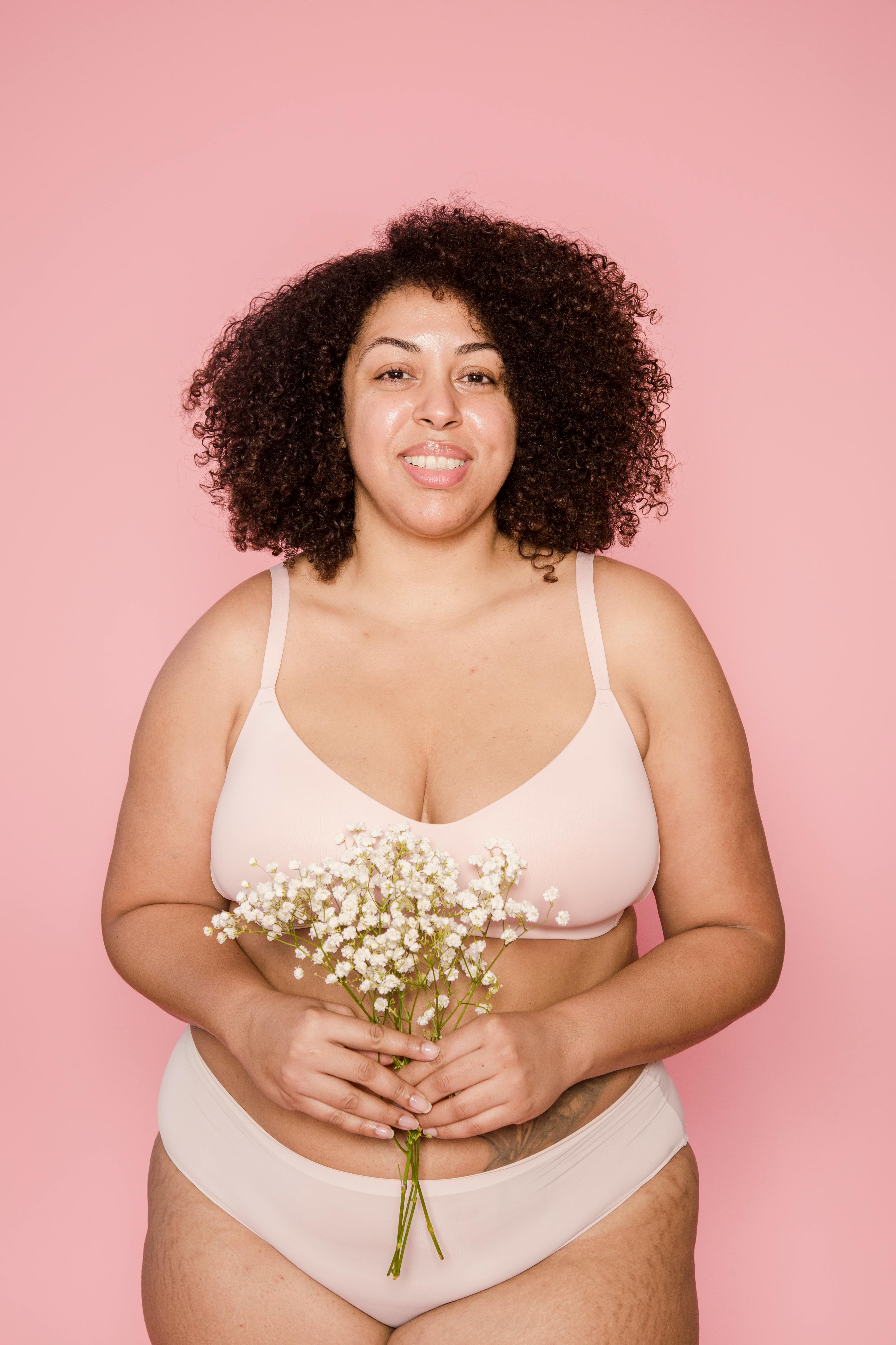 Cheerful overweight black woman in lingerie with flowers in studio