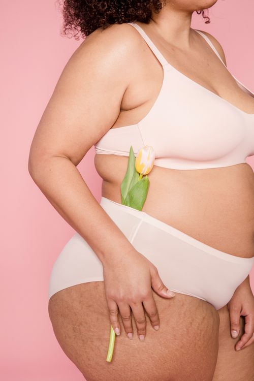 Free Side view of anonymous plus size African American female in lingerie standing on pink background with flower in panties in studio Stock Photo
