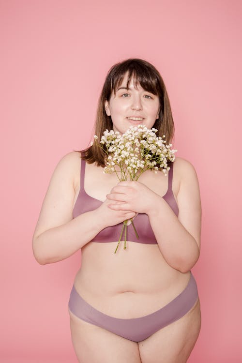 Optimistic plus size Asian woman in underwear with bouquet in hands