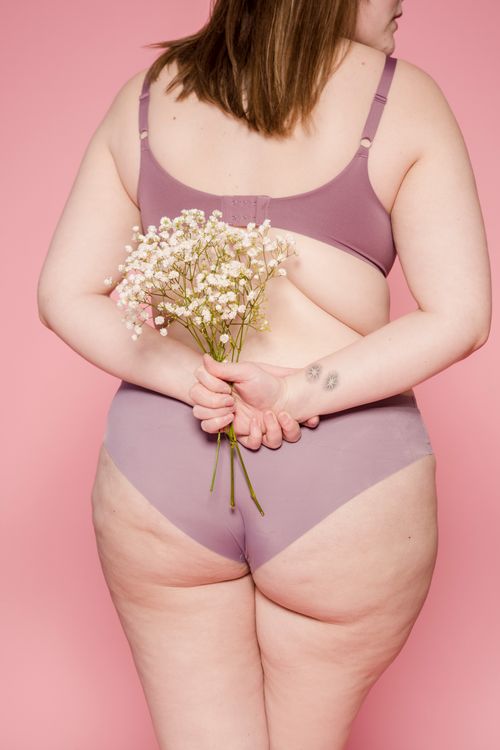 Free Back view of unrecognizable plump female in lingerie with bouquet of fresh small flowers in hands standing on pink background Stock Photo
