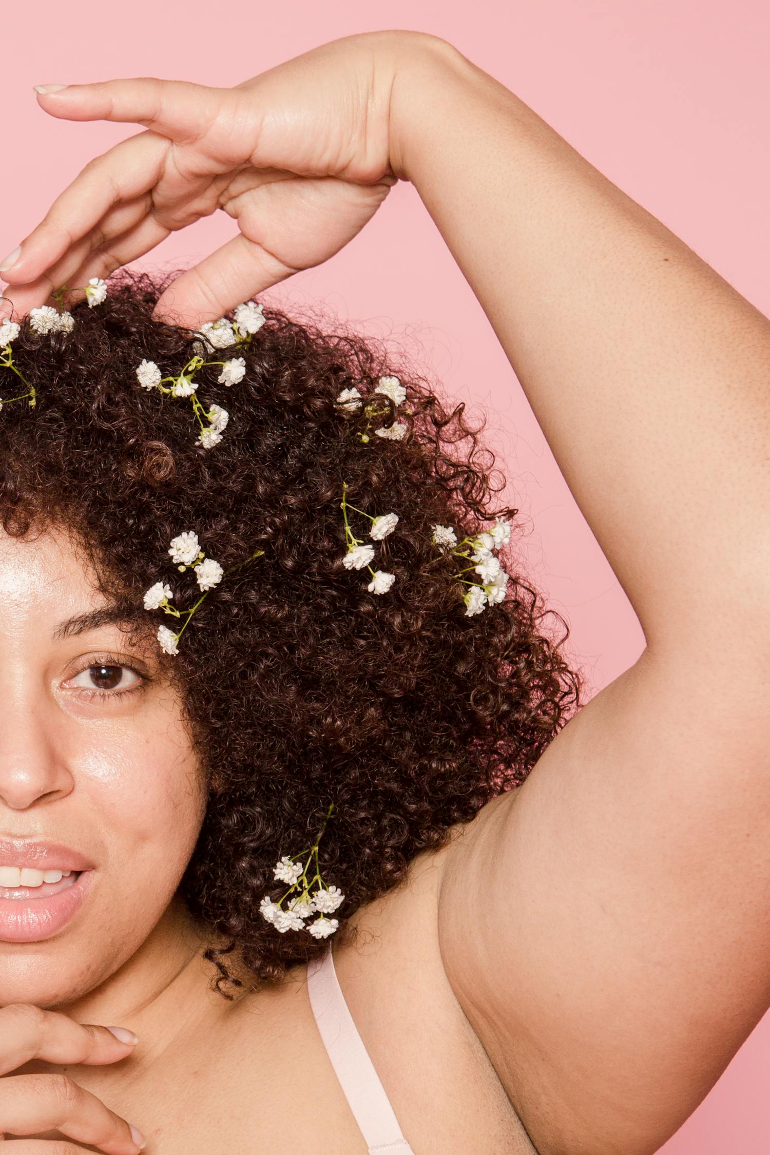 Crop content overweight African American female model with creative small flowers in black hair looking at camera with raised arm on pink background