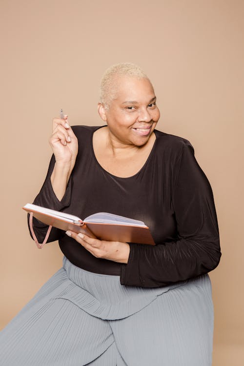 Smiling plump African American female with pen and opened notepad looking at camera on beige background in modern light studio