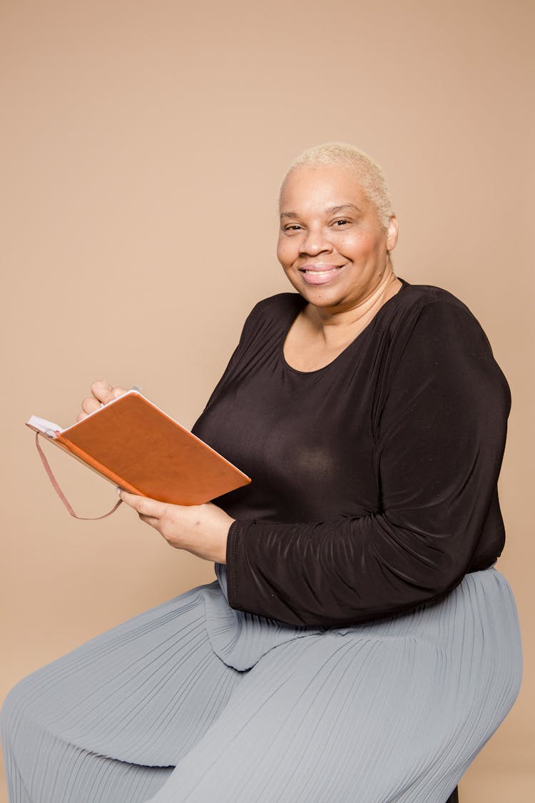 Cheerful Overweight Black Woman Writing In Notebook