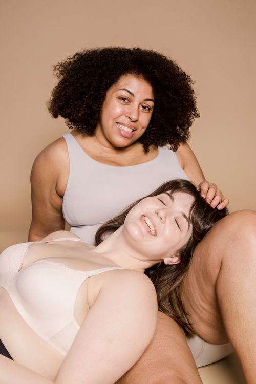 Free Cheerful plus size Asian woman with closed eyes in lingerie lying on legs of plump African American female on beige background Stock Photo