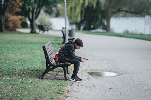 Teenage boy using smartphone on park bench