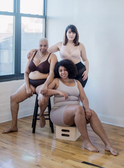 Free Plus size multiracial girlfriends in underwear looking at camera against window and wall in building Stock Photo