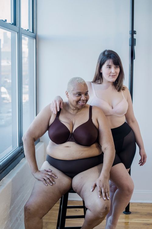 Free Young woman embracing cheerful plus size mature African American model in underclothes while looking away indoors Stock Photo