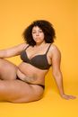 Overweight African American female in bra and panties with curly hair looking at camera on yellow background