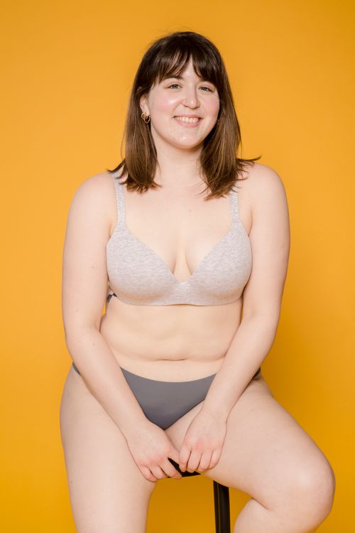 Free Cheerful overweight woman in brassiere and panties looking at camera while sitting on stool on yellow background Stock Photo