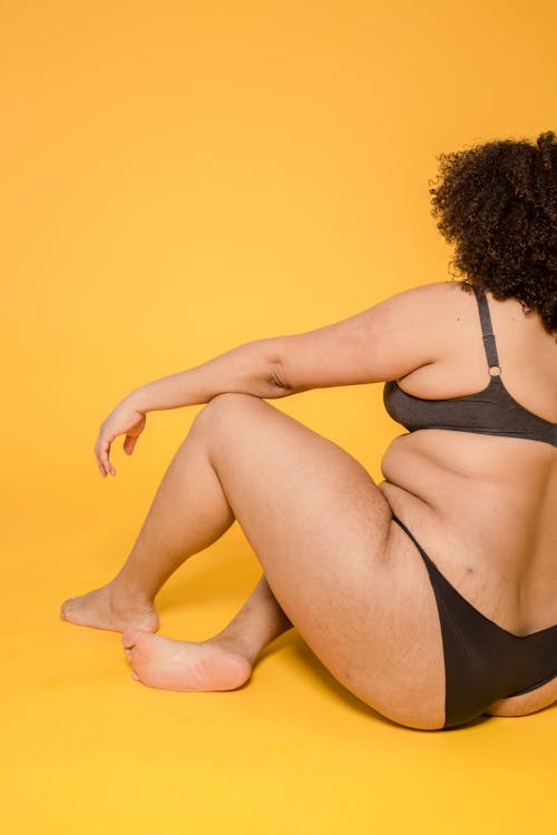 Back view of crop unrecognizable plus size female in bikini and brassiere with curly hair on yellow background