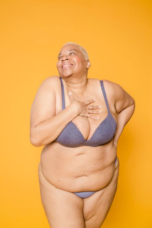 Free Joyful plus-size woman posing confidently in lingerie against a vibrant yellow background. Stock Photo