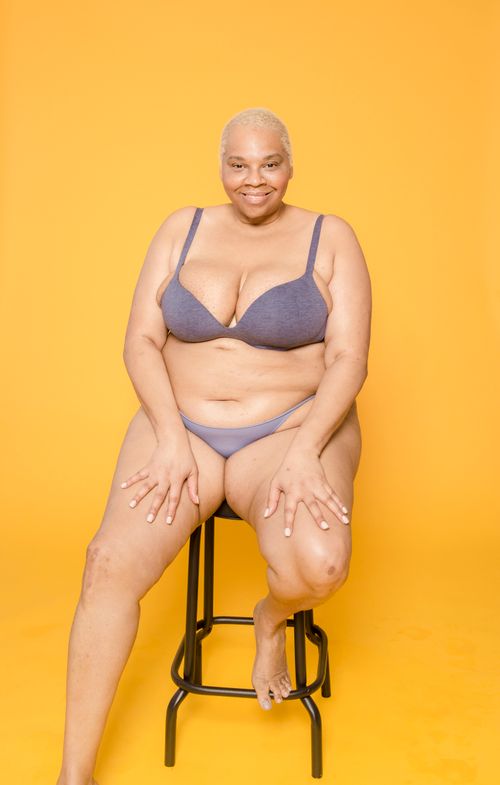 Free A smiling woman in underwear poses confidently on a stool against a vibrant yellow background. Stock Photo