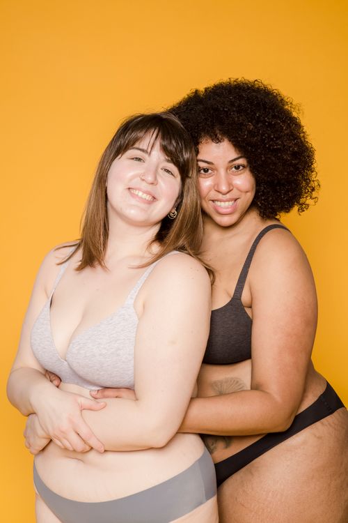 Free Two diverse women in underwear, smiling and embracing against a vibrant yellow background. Stock Photo