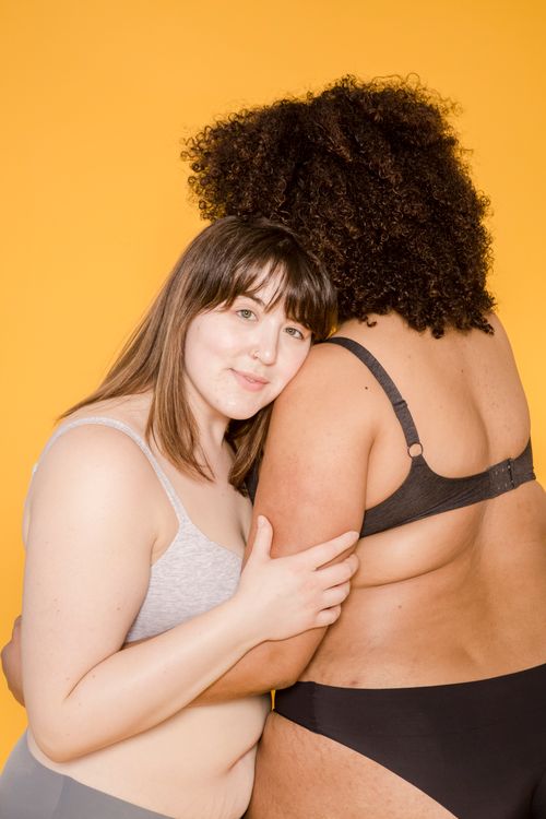 Free Two diverse women embracing in underwear showcase body positivity on a vibrant yellow background. Stock Photo