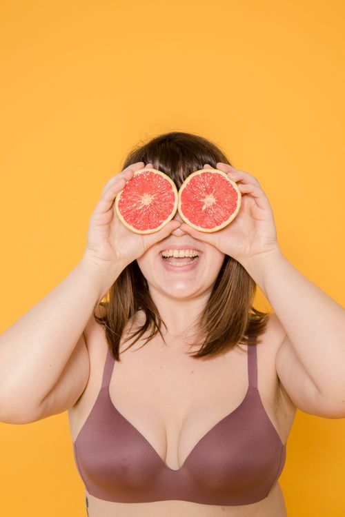 Free Joyful woman holding halved grapefruits over her eyes against a vibrant yellow background. Stock Photo