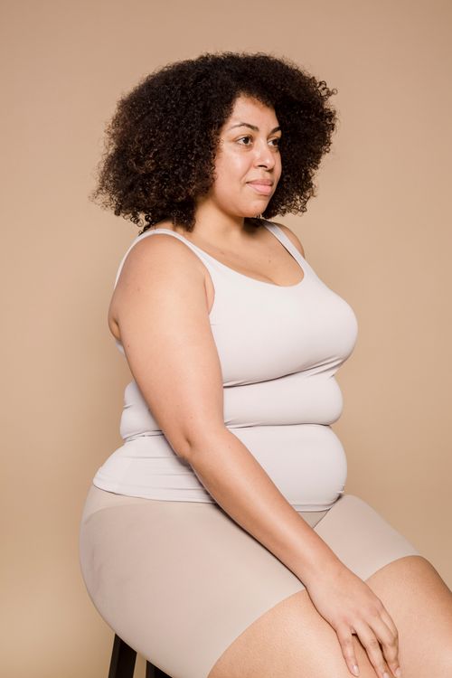 Free Plus size African American female with Afro hairstyle sitting on stool in studio against beige background and looking away Stock Photo