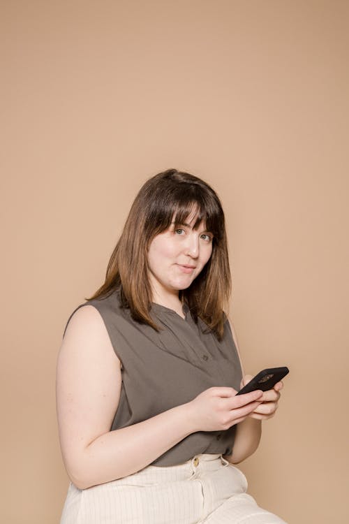 Smiling woman in casual outfit browsing smartphone in studio