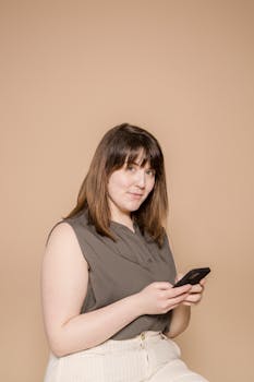 Smiling young woman casually browsing on smartphone in a studio setting.