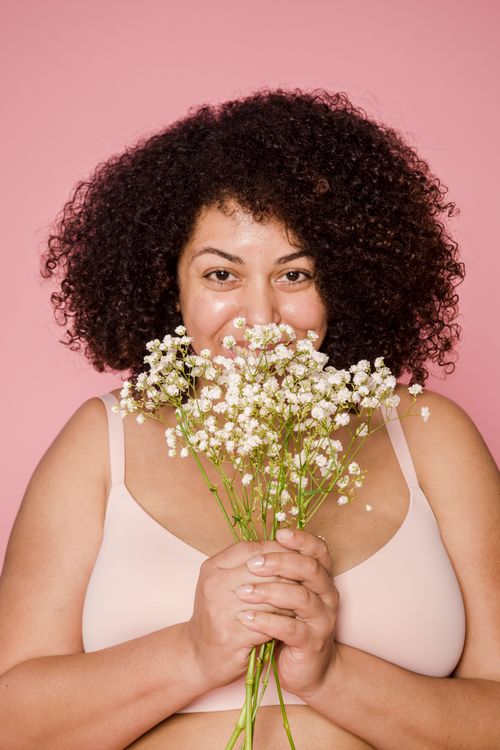 Free Positive overweight African American female with curly hair wearing bra smiling bouquet of fresh flowers against pink background and looking at camera Stock Photo