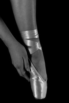Close-up of a dancer adjusting a pointe shoe in an elegant black and white photo.