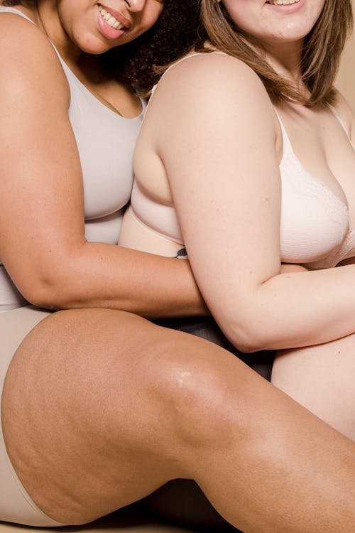 Free Side view of crop cheerful multiethnic female plus size models wearing underwear cuddling together Stock Photo
